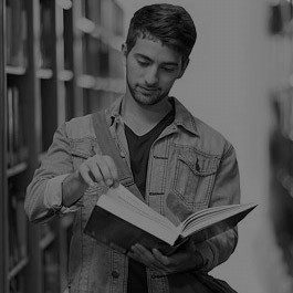  Junger Mann blättert in einem Buch zwischen Bücherregalen. 
