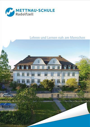  Frontansicht eines großen weißen Gebäudes mit mehreren Fenstern und einem braunen Dach, umgeben von Bäumen, mit der Aufschrift „METTNAU-SCHULE Radolfzell“ am oberen Rand. 